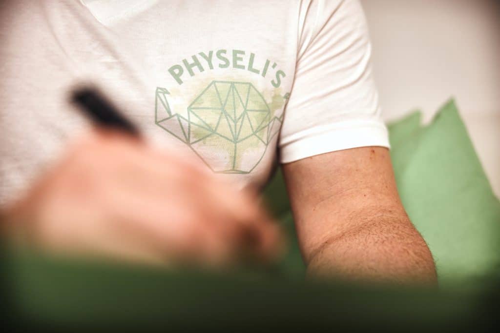 Physeli's Mitarbeiter mit Physeli's Logo T-Shirt notiert etwas im Ernährungsplan.